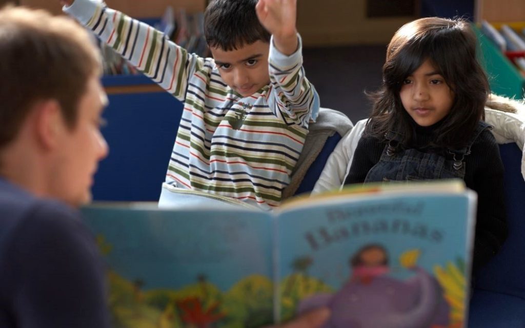 Photo of an adult man reading a book to two children.