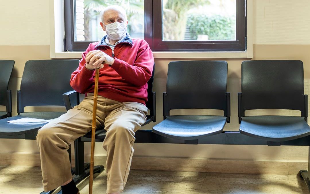 Photo of an older man wearing a face covering, waiting in a doctors' surgery.