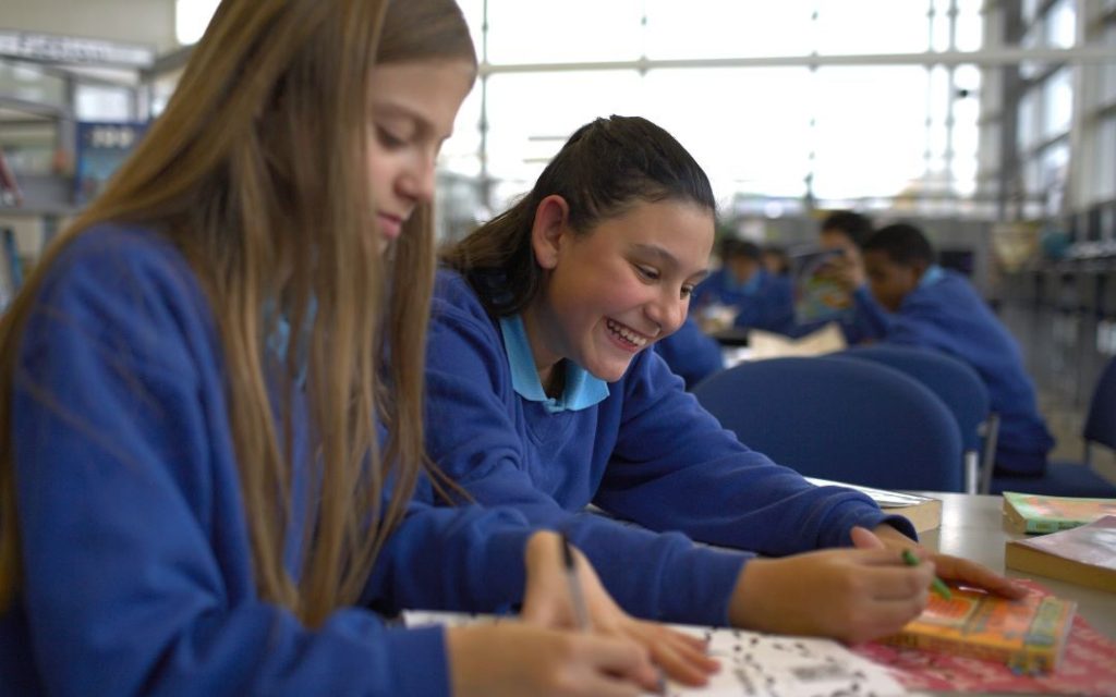Photo of two girls in school uniform reading books and smiling